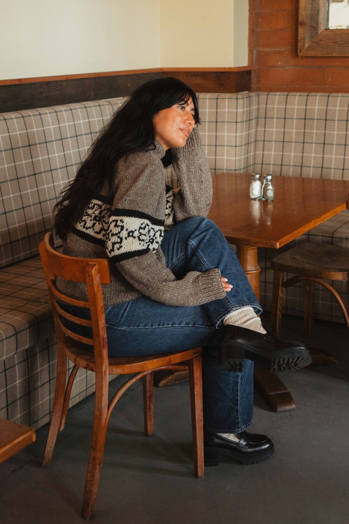Side view of the knit flower sweater sleeve band, model seated on a wooden chair