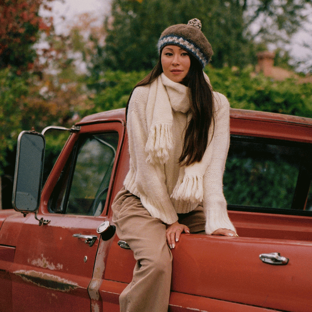 woman sitting in back of red truck wearing a white sweater, scarf and knit beret
