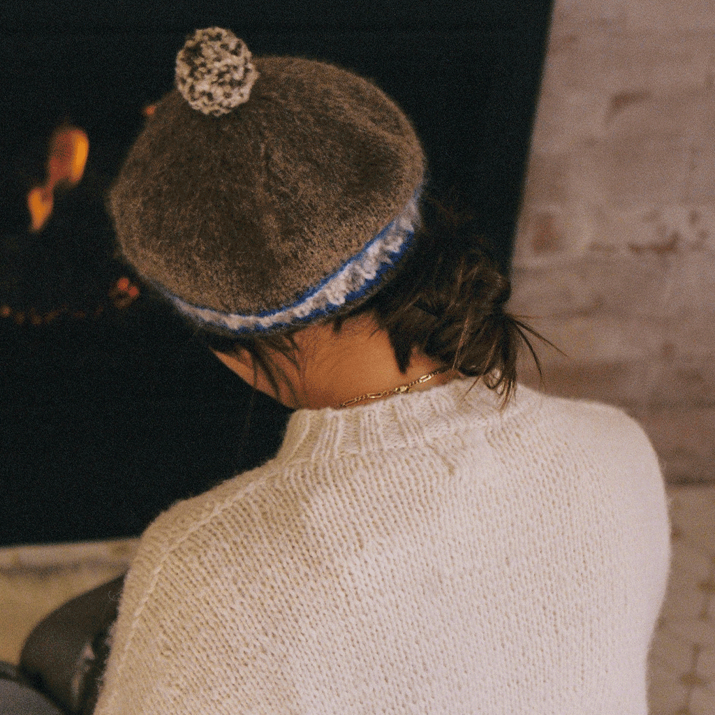 woman wearing white sweater and grey beret in front of a fire