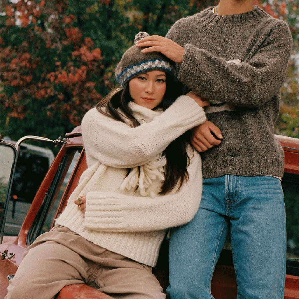 woman wearing white sweater and grey beret, she is in the back of a red truck, sitting next to another person