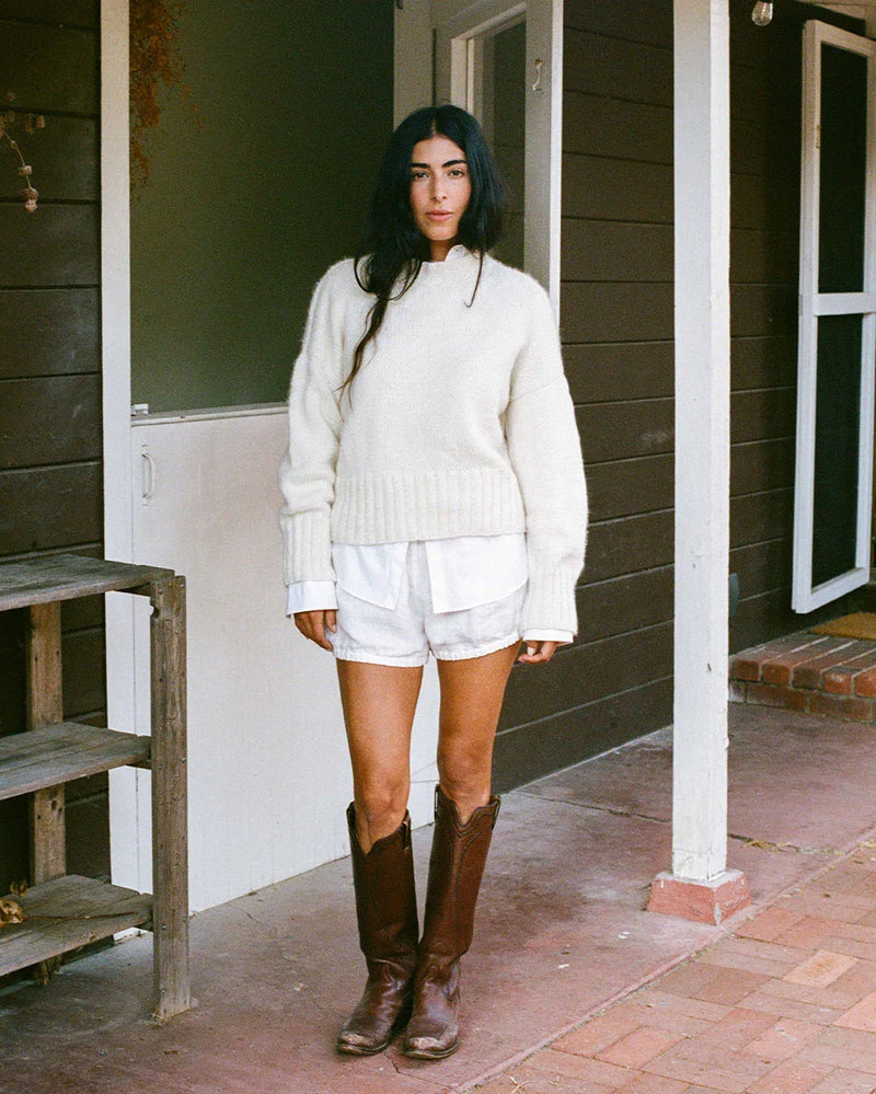 Woman in a cream hand-knit alpaca sweater standing on a porch