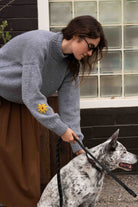 Banjo Blue alpaca wool sweater with hand-embroidered yellow flower on the sleeve, worn while walking a spotted dog