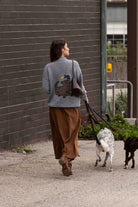 Back view of the Banjo Blue Best Buds sweater with dog and bird graphic, walking two dogs along a brick wall
