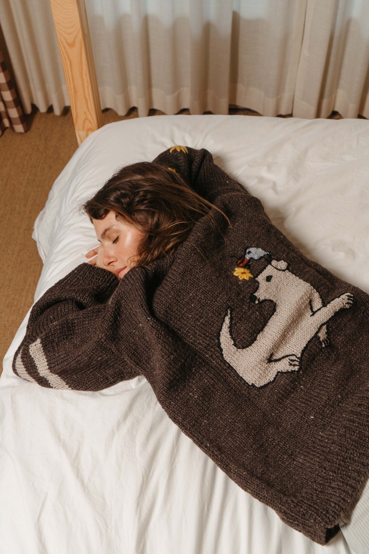 Buster Brown Best Buds hand-knit sweater worn lying on a bed, showing the cream dog and bird graphic on the back