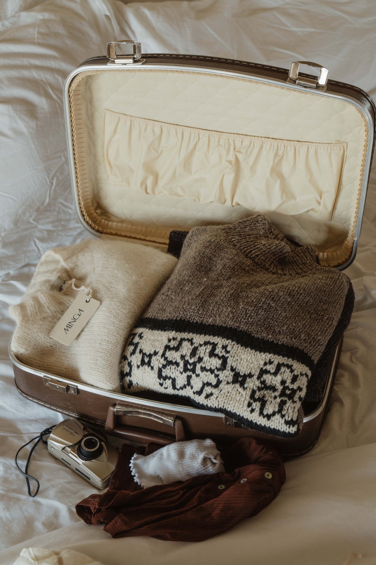 Gray hand knit flower sweater folded in a vintage suitcase with a cream knit and a film camera