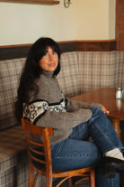 Model sitting in a diner booth wearing the gray Fair Isle style flower sweater with jeans