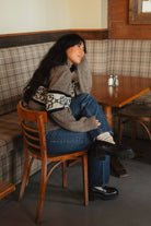 Side view of the knit flower sweater sleeve band, model seated on a wooden chair