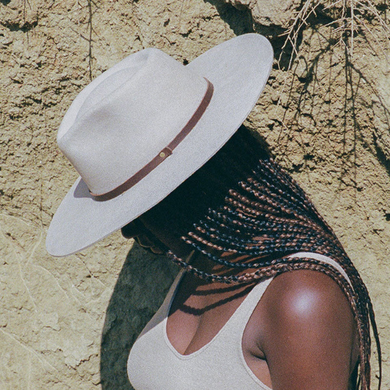 Woman in a white wide-brim wool hat standing against an adobe wall